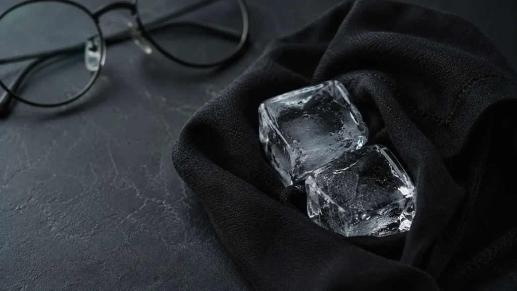 Dois cubos de gelo minimalistas e cristalinos envoltos em um pano preto de algodão premium, sobre uma superfície de pedra escura.